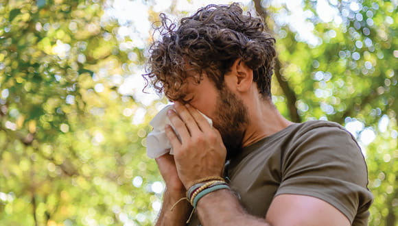 A man sneezes because of Houston allergies as he hikes in a wooded area during the spring.