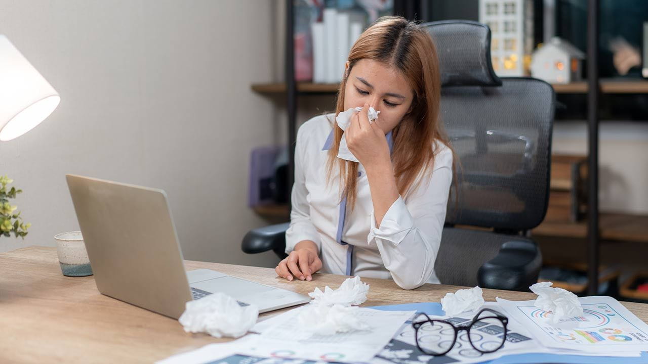 A woman blows her nose as she works while sick. 