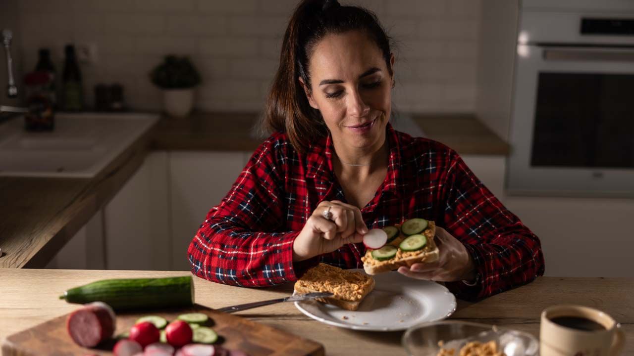 A woman makes a low-energy meal of an easy toast with spread, cucumbers and radishes. 