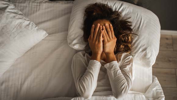 A woman covers her face after getting a poor night's sleep due to sleep apnea symptoms.