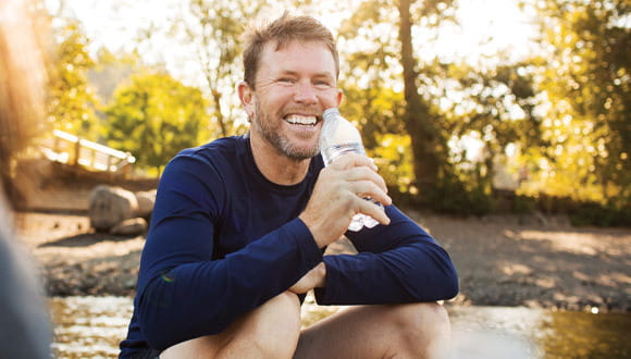 An active man sits and drinks water while smiling
