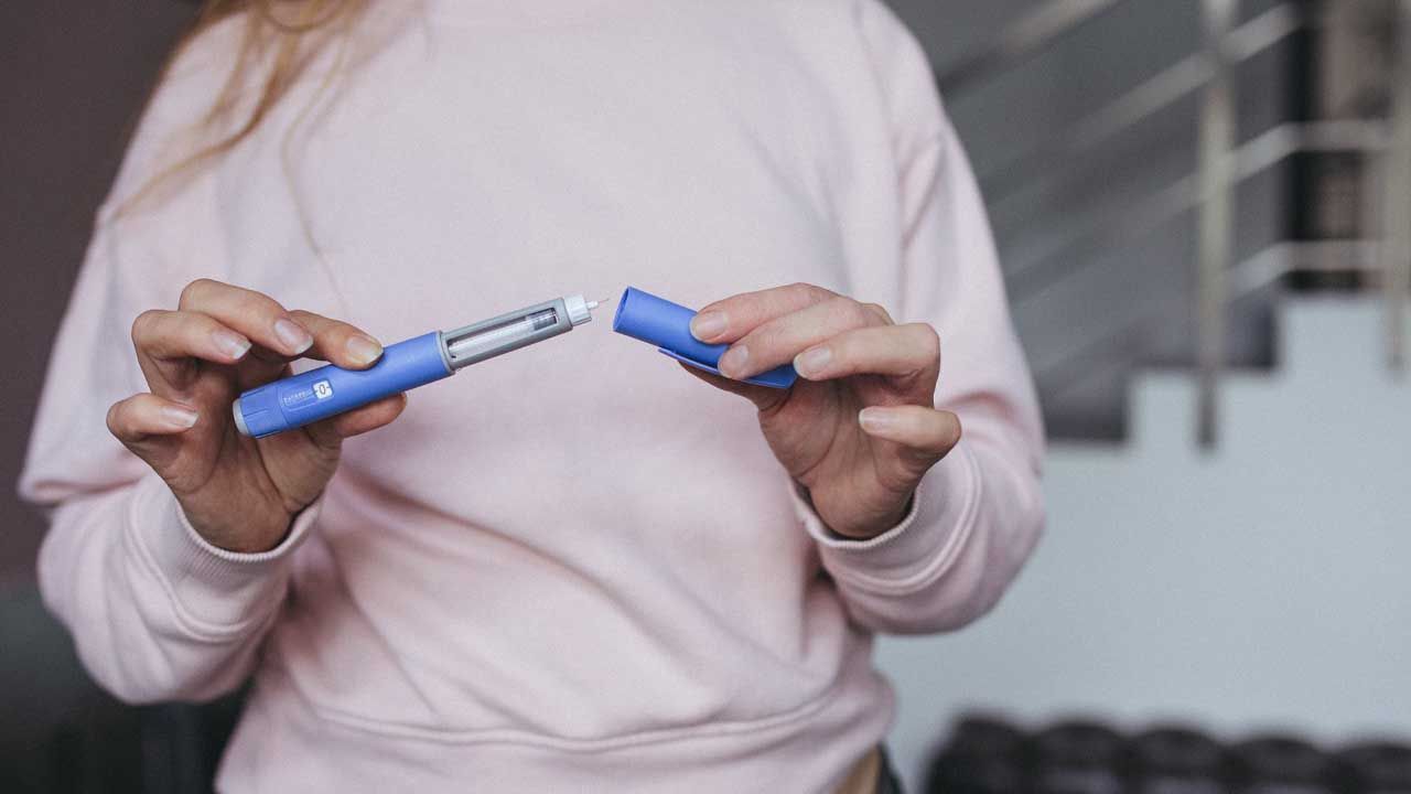 Person holding an injectable weight-loss medication pen with the cap removed.