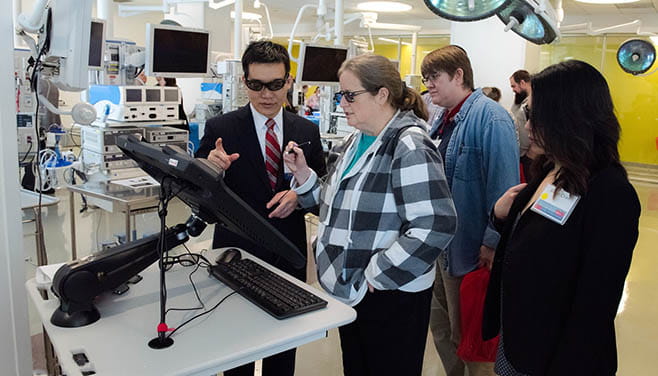 Both wearing light filtering glasses, a demonstrator shows an attendee at the Adult Congenital Heart Symposium how to use a heart monitoring computer device.