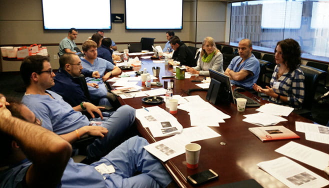 A group of cardiovascular fellows and an instructor sit around a table editing their manuscripts as a group. 