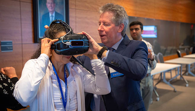 A man in a suit helps a woman adjust virtual reality goggles.