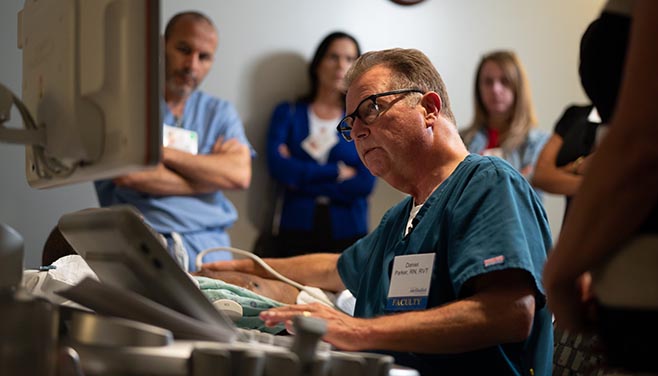 A male nurse uses an ultrasound machine to examine a patient while looking at a computer monitor.