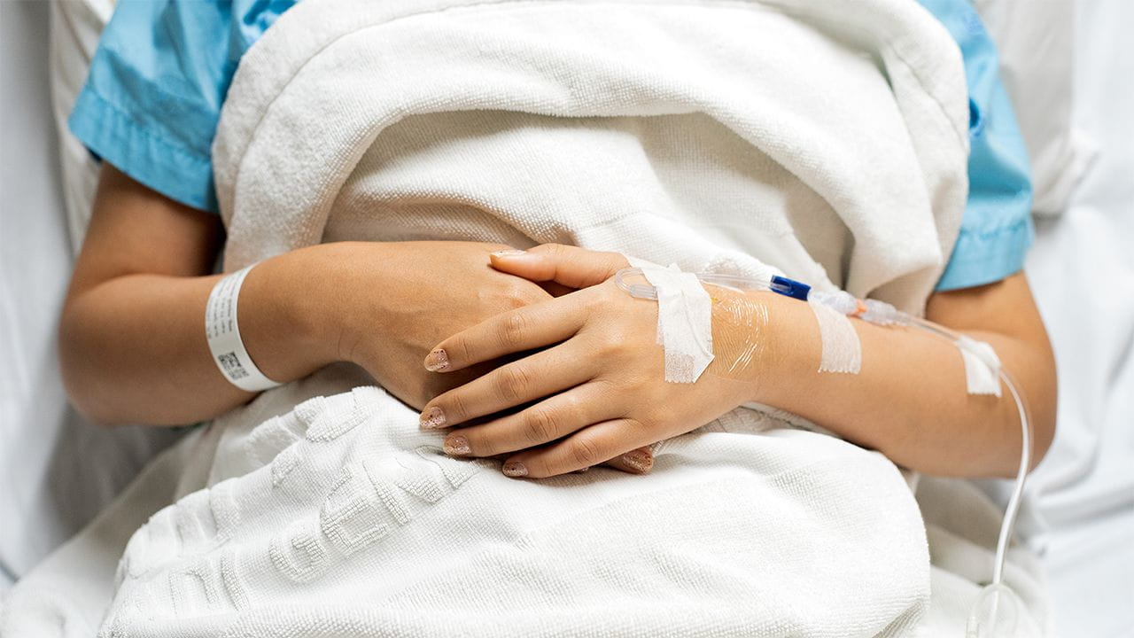 A close up image of a woman in a surgical bed from above the bed. She has her hands folded over her abdomen and a white blanket covering her up to her shoulders.