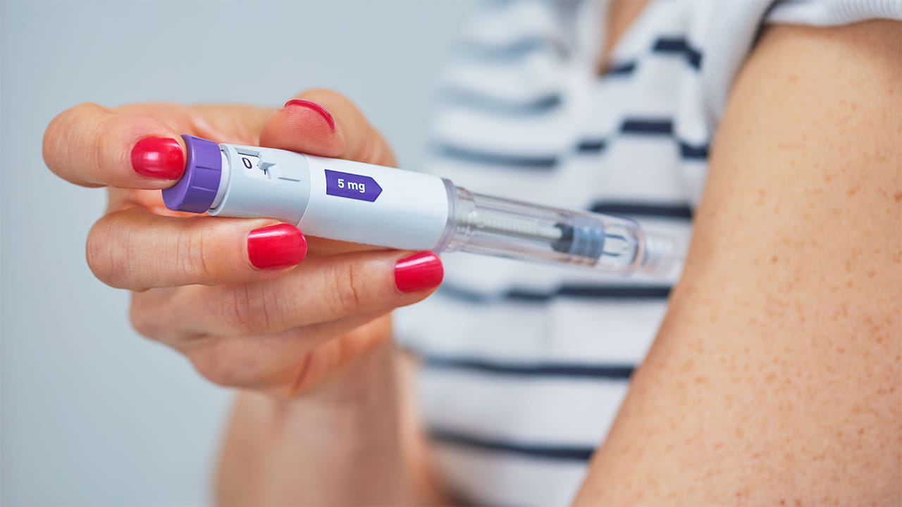 A closeup of a female's upper body showing a GLP-1 like injection pen about to go into the upper arm.