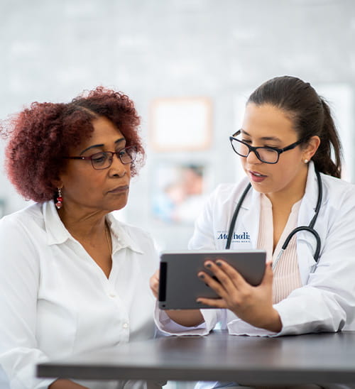 Houston Methodist healthcare provider in a white coat reviewing information on a tablet with a patient seated at a table during a medical consultation.
