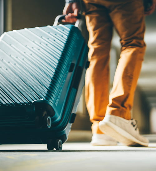Close-up of a traveler pulling a wheeled suitcase across a walkway, highlighting movement and travel.