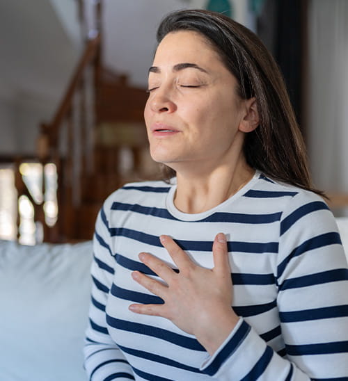 Person seated at home with a hand on the chest, representing shortness of breath, a potential cardiovascular or respiratory symptom.