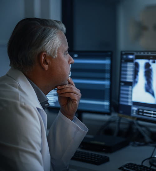 Healthcare professional seated at a workstation, reviewing chest imaging displayed on multiple computer monitors in a medical setting.
