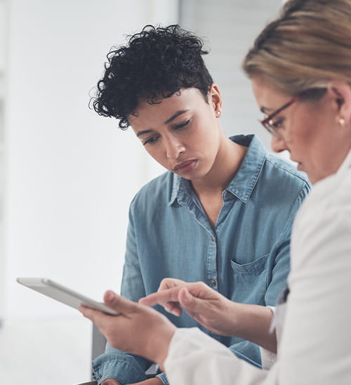 Healthcare provider using a tablet to explain treatment information to a patient during a clinical consultation.