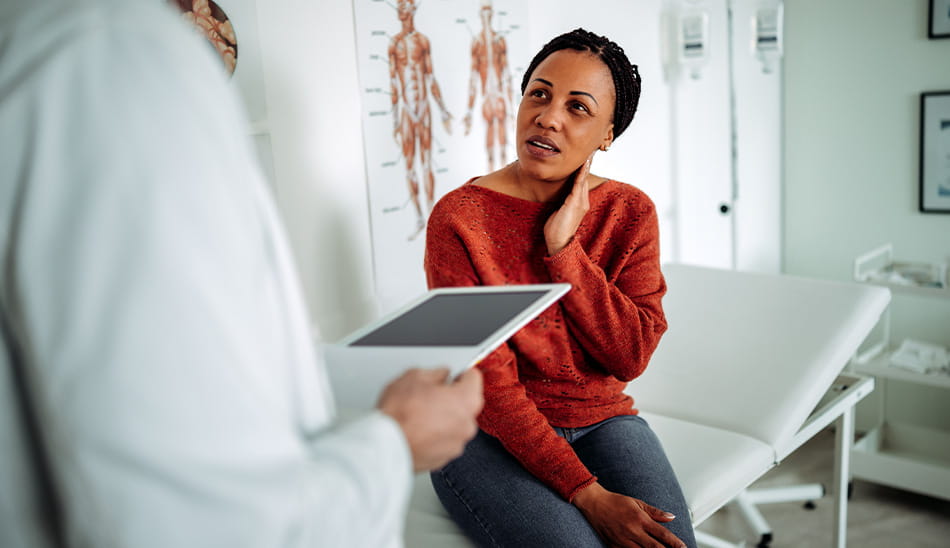 Woman holding her neck in pain while talking to a doctor.