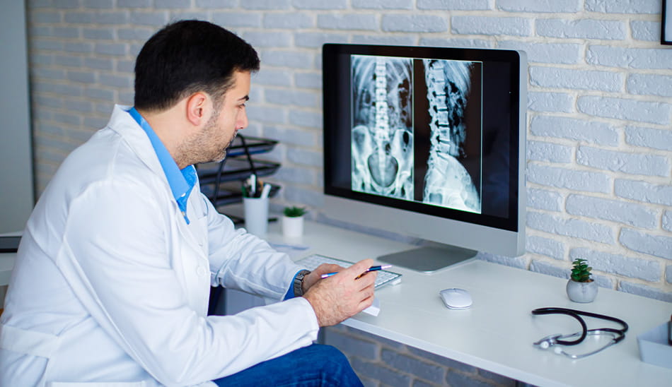 Doctor analyzing a spinal X-ray on a computer screen for a patient.
