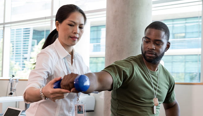 female physical therapist helping a young male patient lift dumbbells