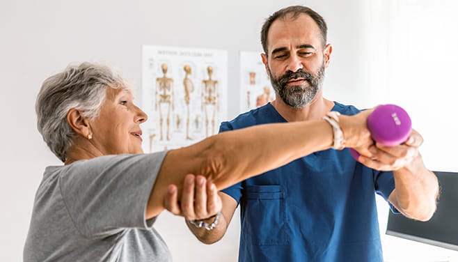 male physical therapist helping elderly female patient lift dumbbells